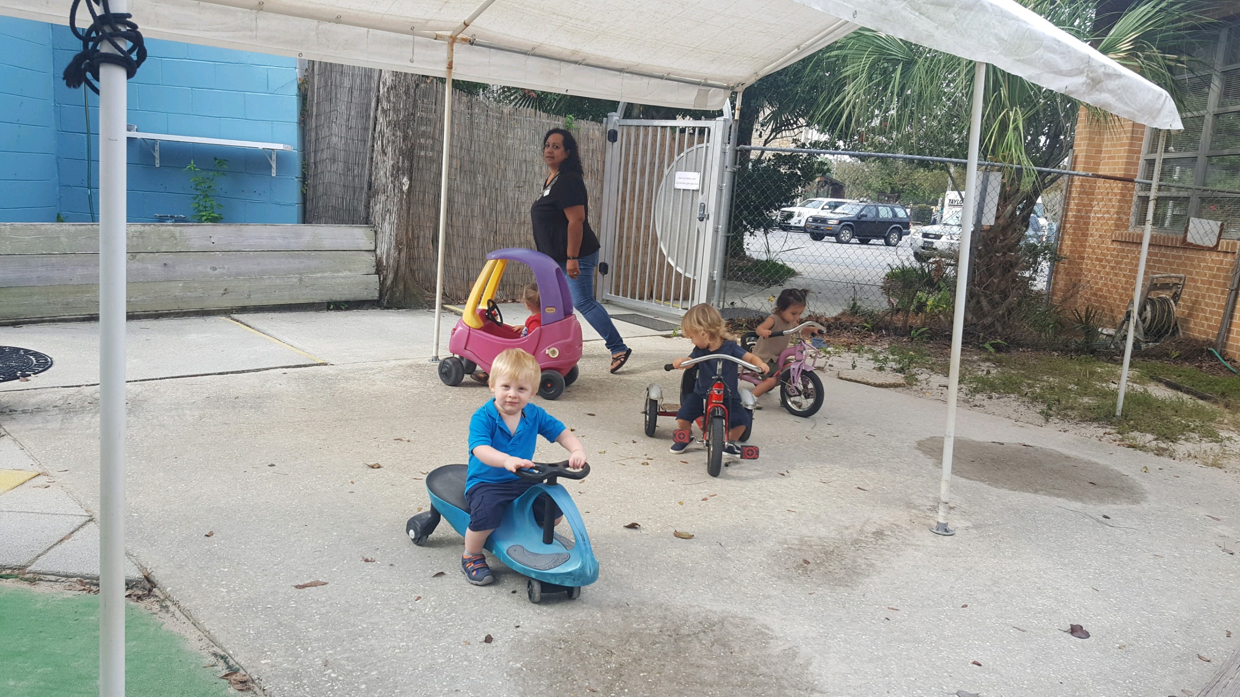 Toddler Montessori students riding cars and tricycles at recess