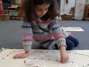 Montessori student on a mat working with a bead activity